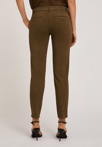 Pantalones marrones ajustados, hechos de una tela suave, con una cintura de altura media, bolsillos traseros y piernas ajustadas, combinados con zapatos de tacón altos negros.