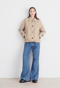 Beige quilted jacket with a collar, featuring diamond patterns and brown buttons. Paired with light blue flared jeans and black shoes.