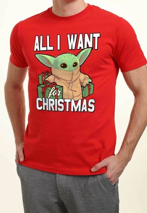 Czerwona bawełniana koszulka z nadrukiem postaci z kreskówki o zielonej skórze, dużych uszach i zapakowanych prezentach, z napisem "WSZYSTKO, CZEGO CHCĘ NA ŚWIĘTA" napisanym na pogrubieniu.