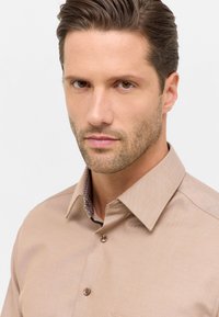 Beige knap-up skjorte med et struktureret stof, der har en mønstret indvendig krave og to brune knapper foran.