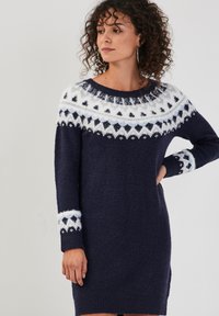 Robe pull en maille bleu marine avec un col rond, présentant un empiècement et des poignets à motifs blancs et bleu clair. Tissu doux et texturé.