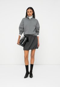 Γκρι sweatshirt με μισό φερμουάρ στον γιακά, συνδυασμένο με μαύρη, πλισέ μίνι φούστα. Μαύρη, λαμπερή τσάντα χεριού και μαύρες κάλτσες με μυτερά τακούνια.