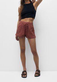 Zwarte cropped tanktop, rustkleurige shorts met trekkoord van een gestructureerde stof en bruine sandalen met straps. Eenvoudige, casual outfit.