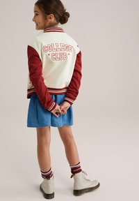 Vårjacka i krämfärg med vinröda ärmar, texten "COLLEGE CLUB", matchad med en jeanskjol och vita kängor med röda strumpor.