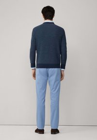 Mornarica pulover s teksturiranim završetkom, okruglim izrezom i rebrastim rubom, uparen sa svijetloplavim hlačama. Smeđi cipele su vidljive pri dnu.