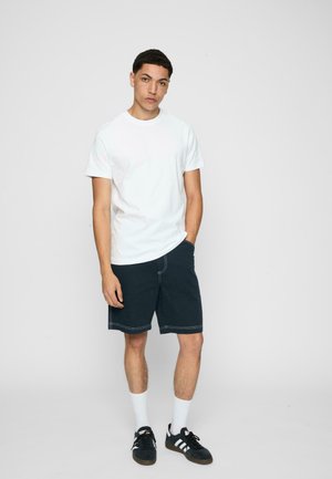 Hvid bomulds t-shirt, mørkeblå shorts med hvid syning, hvide ankelstrømper og sorte sneakers. Enkel, afslappet stil med en løs pasform.