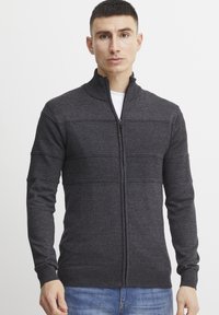 Sweater zippé gris foncé avec des rayures horizontales texturées et des poignets et un ourlet côtelés, fabriqué en maille douce.