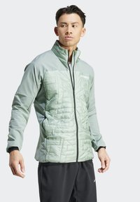 Chaqueta aislante de color verde claro con frente acolchado, cuello alto y cremallera de longitud completa; acentos negros contrastantes en las mangas y el ribete.
