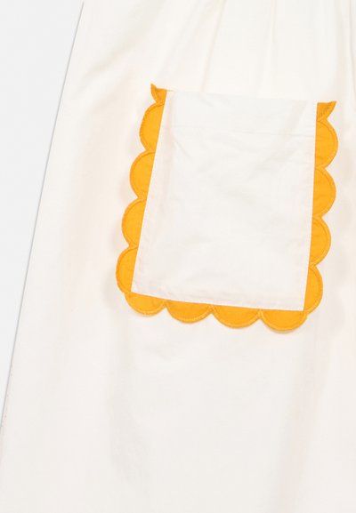 Biely textil s obdĺžnikovou vreckom ohraničeným žltým zvlneným lemom v tvare kvetových lupienkov.