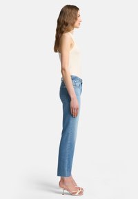 Ljusblå raka jeans med rå fåll, i kombination med en åtsittande beige linne och vita högklackade sandaler med remmar.