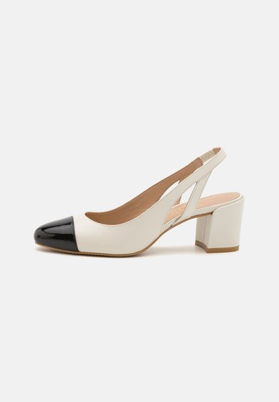 Chaussure slingback en cuir blanc avec un bout pointu en cuir verni noir. Elle présente un talon bloc et un design découpé sur les côtés.