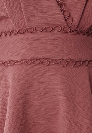 Tkanina boje maline s teksturiranim površinom. Ima šivene okrugle detalje duž linije struka, stvarajući suptilan dizajnerski element.