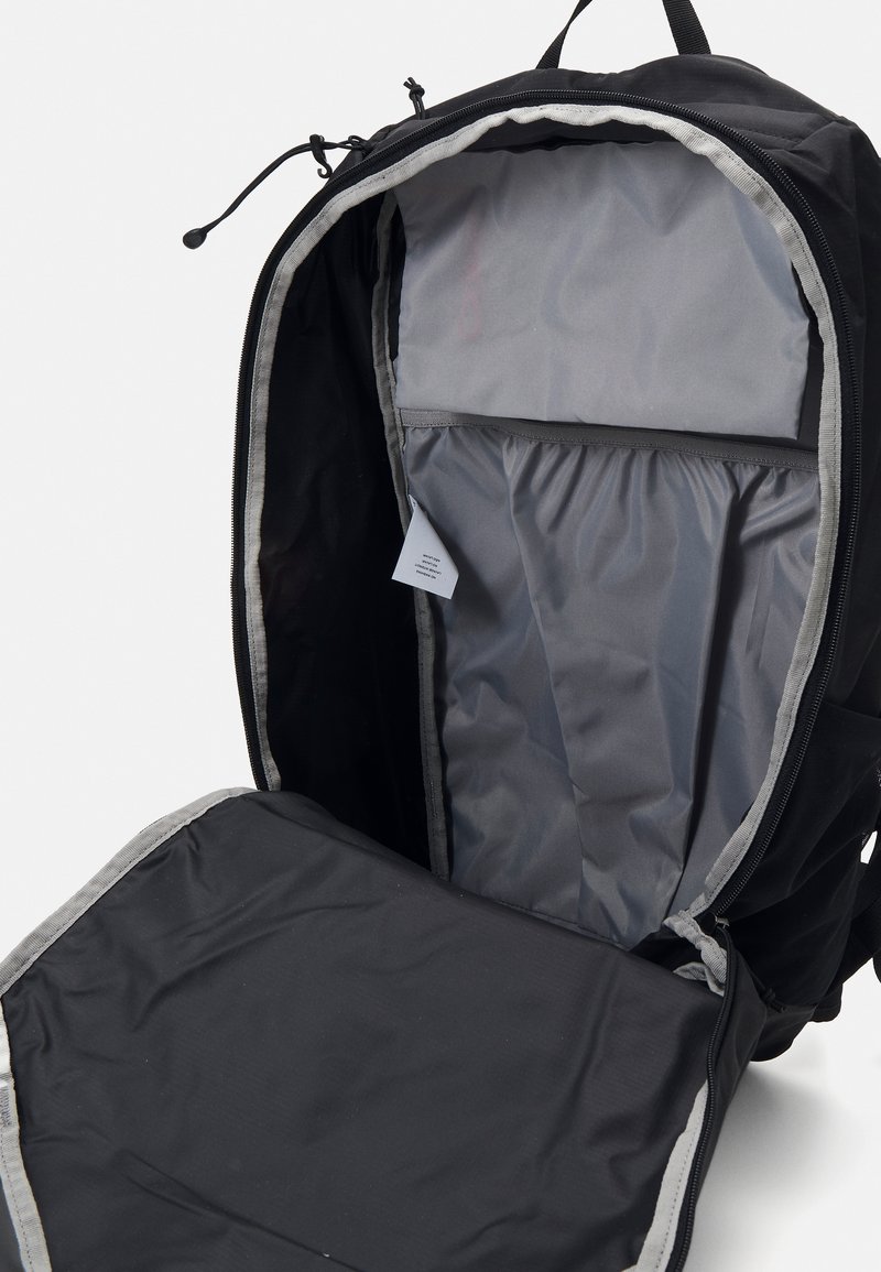 Sac à dos noir avec doublure grise, présentant un intérieur spacieux et une poche zippée. Texture lisse et tissu durable.