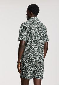 Kurze Ärmel Hemd und Shorts Set in grün-weißer abstrakter Musterung, aus leichtem Stoff gefertigt. Verfügt über einen Kragen und eine aufgesetzte Tasche.