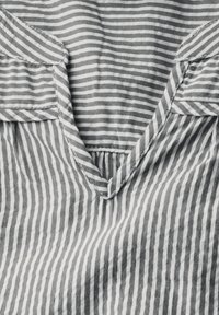 Tissu rayé avec des lignes grises et blanches alternées. Présente un col en V et une texture décontractée. Détails de couture minimaux visibles.