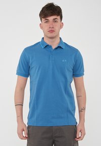 Polo shirt blu realizzato in cotone, con colletto e polsini di un azzurro a contrasto, e un piccolo logo sul petto. Maniche corte.