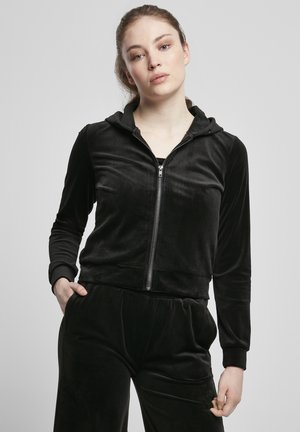 Sudadera con cremallera de terciopelo negro, con un diseño ajustado, mangas largas y capucha. Presenta una textura suave y puños elásticos.