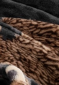 Faux fur tæppe med en blanding af sort, brunt og creme teksturer samt dyreprint mønstre, blød og luksuriøs overflade.