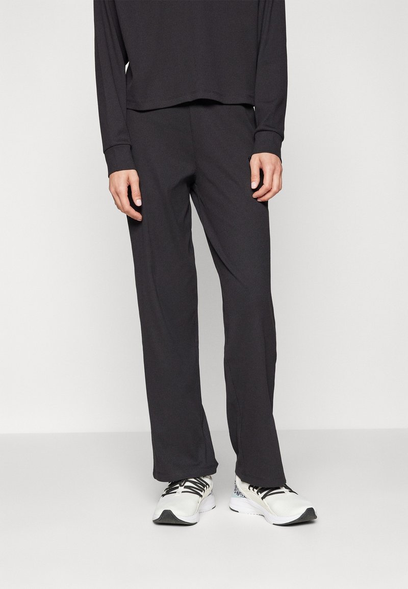 Black ribbed long-sleeve top paired with matching loose-fitting pants. Worn with white athletic shoes featuring black accents.