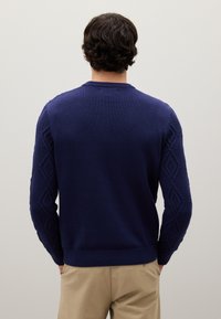 Dunkelblau gestrickter Pullover mit einem strukturierten Rautenmuster an den Ärmeln, Rundhalsausschnitt und ribbeligem Saum. Glatter Körper mit kontrastierenden Details.