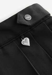 Zwarte stof met een gestructureerde afwerking, voorzien van een zilveren knop met het label "Clarks" en een zilveren hartvormige hanger die aan een zwarte band is bevestigd.
