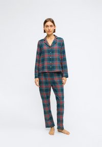 Károvaná pyžamová súprava v tmavozelenej, červenej a modrej farbe, obsahujúca košeľu na gombíky s golierom a voľné nohavice s elastickým pásom.