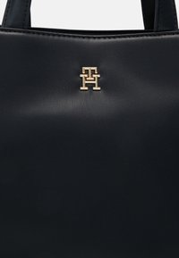 Navy Lederhandtasche mit strukturiertem Finish und einem goldenen Logoakzent in der Mitte der Vorderseite. Zwei Handgriffe oben runden das Design ab.