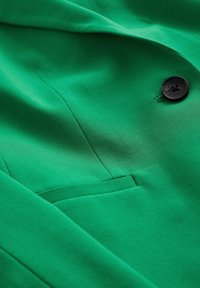 Grön blazer i ett slätt tyg med en svart knapp och en sidficka, med en ren skräddarsydd stil och en strukturerad silhuett.