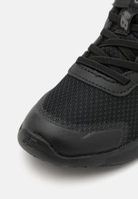 Black athletic shoe featuring a mesh upper, smooth rubber toe cap, textured laces, and subtle branding on the side.