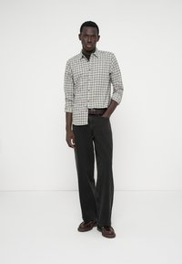 Gray and white checkered button-up shirt with rolled sleeves, paired with black straight-leg jeans and brown shoes.