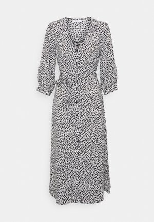 Vestido de patrón en blanco y negro con escote en V, mangas largas, botones en el frontal y cintura con lazo. Confeccionado en una tela ligera y fluida.