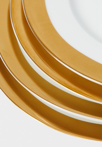 Hrpa od tri bijela tanjura s širokim zlatnim rubovima, postavljena po silaznom redoslijedu veličine na bijeloj površini.