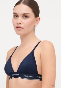 Navyfarbener dreieckiger BH aus glattem Stoff mit einem elastischen Band mit weißer Beschriftung und dünnen verstellbaren Trägern.