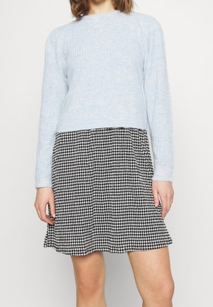 Suéter de canalé azul claro con mangas largas, combinado con una falda de pata de gallo en blanco y negro que presenta pliegues y un dobladillo acampanado.