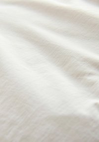 Helle cremefarbene Stoff mit einem subtilen strukturierten Muster, das glatt und leicht zerknittert erscheint und seine weiche, natürliche Textur unterstreicht.