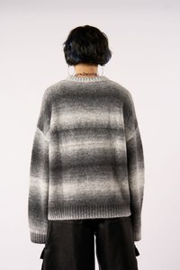 Grå strikket sweater med et gradientmønster, ribbet kant og brede ærmer. Sammen med sorte bukser, der har en struktureret finish.