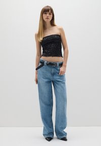 Top negro sin mangas con textura fruncida, combinado con jeans de pierna ancha de color azul claro y un cinturón negro. La modelo lleva puestos tacones negros de punta.