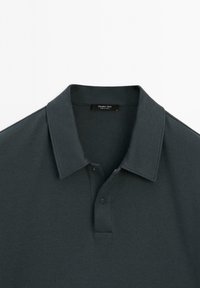Mörkgrå polo med klassisk krage, tvåknäppning och mjukt tyg. Märkningen säger "Massimo Dutti". Enkel och strömlinjeformad design.