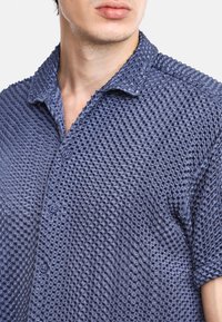 Camisa de manga corta en azul marino, hecha de una tela texturizada con un patrón acanalado, que cuenta con un cierre de botones en la parte delantera y un cuello puntiagudo.