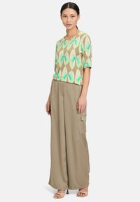 Short-sleeve top with a green, brown, and aqua geometric pattern, paired with light brown wide-leg pants featuring cargo pockets.