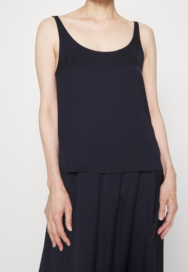 Granatowy bezrękawnik wykonany z miękkiego materiału, z okrągłym dekoltem i luźnym krojem, zestawiony z luźnymi ciemnymi spodniami.