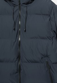 Granatowa ocieplana kurtka z suwakiem z przodu, kapturem z regulowanymi czarnymi sznurkami i zapinaną na zamek kieszenią boczną.