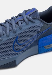 Mørkeblå sportsko med mesh-overdel, der har et struktureret mønster, runde snørebånd og et blankt blåt Swoosh-logo.