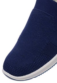 Detailní záběr tmavě modré pletené tenisky slip-on s bílou podrážkou, zobrazující texturovaný pletený vzor a elastický lem u kotníku.