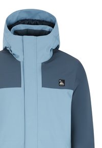 Giacca azzurra chiara con colletto alto, presenta accenti blu scuri e una toppa con logo nera. Texture liscia, materiale impermeabile, design moderno.