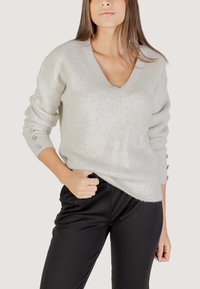Maglione grigio chiaro lavorato a maglia con scollo a V, texture a costine e dettagli con bottoni sulle maniche. Abbinato a pantaloni neri.