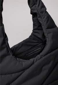 Gros plan sur un sac noir rembourré avec une étiquette visible indiquant qu'il est fabriqué à partir de filets de pêche recyclés.