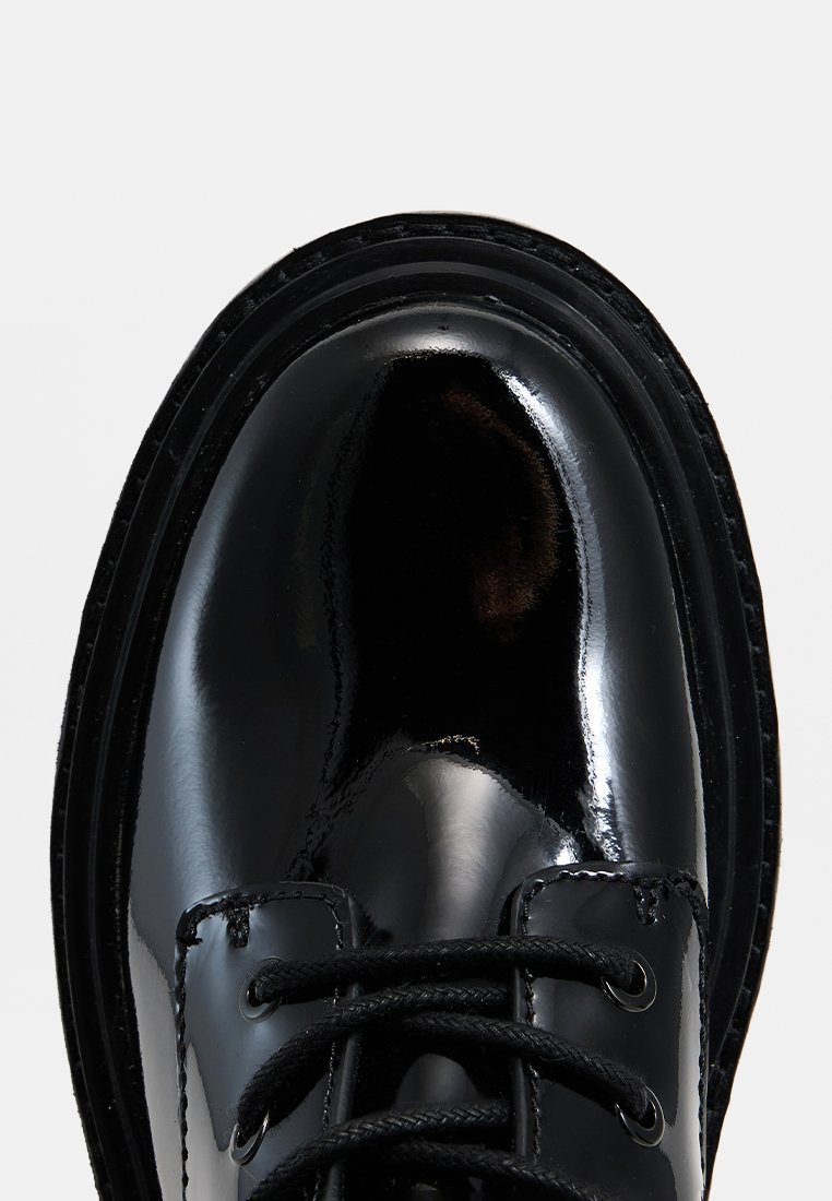Schwarzer Lacklederschuh mit runder Zehenpartie, dicker schwarzer Sohle und schwarzen Schnürsenkeln. Verfügt über eine glatte, glänzende Oberfläche und gestickte Details.