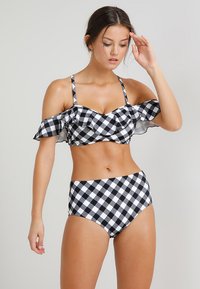 Conjunto de bikini em preto e branco com padrão xadrez, apresentando um top com babados e alças caídas, e partes inferiores de cintura alta, feito de um tecido suave.