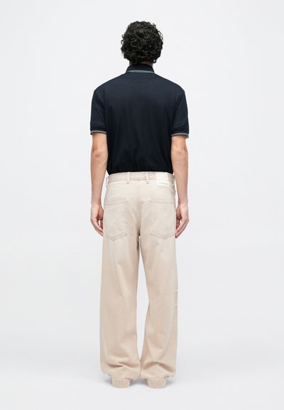 Μπλε ναυτικό πόλο μπλουζάκι με κοντά μανίκια, με γιακά τριών κουμπιών. Συνδυάζεται με μπεζ παντελόνι φαρδιάς γραμμής, με πίσω τσέπες.